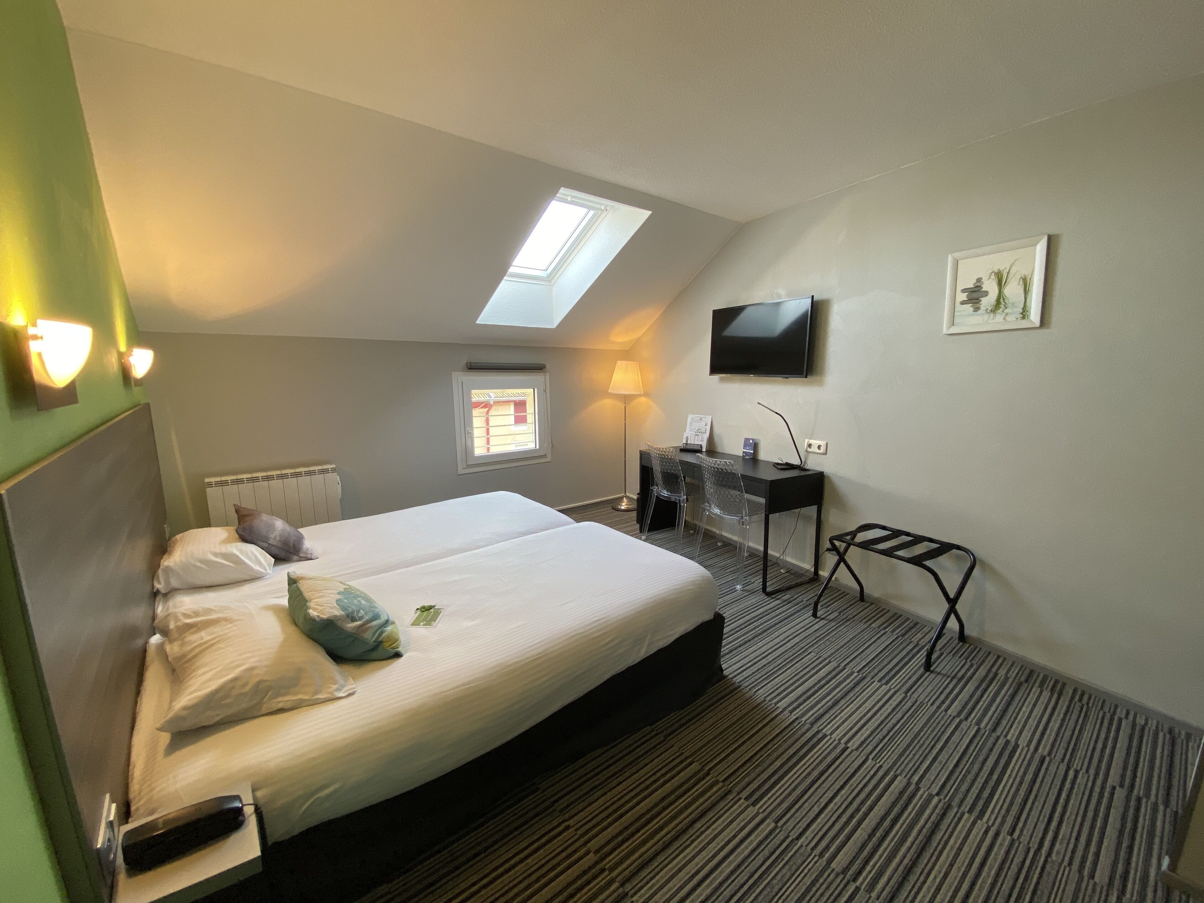 A hotel room with a large bed, a desk with a chair, a TV, and a small window.