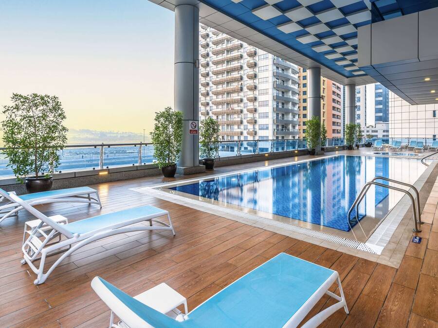 Uma área de piscina com espreguiçadeiras, plantas em vasos e vista para a paisagem urbana.