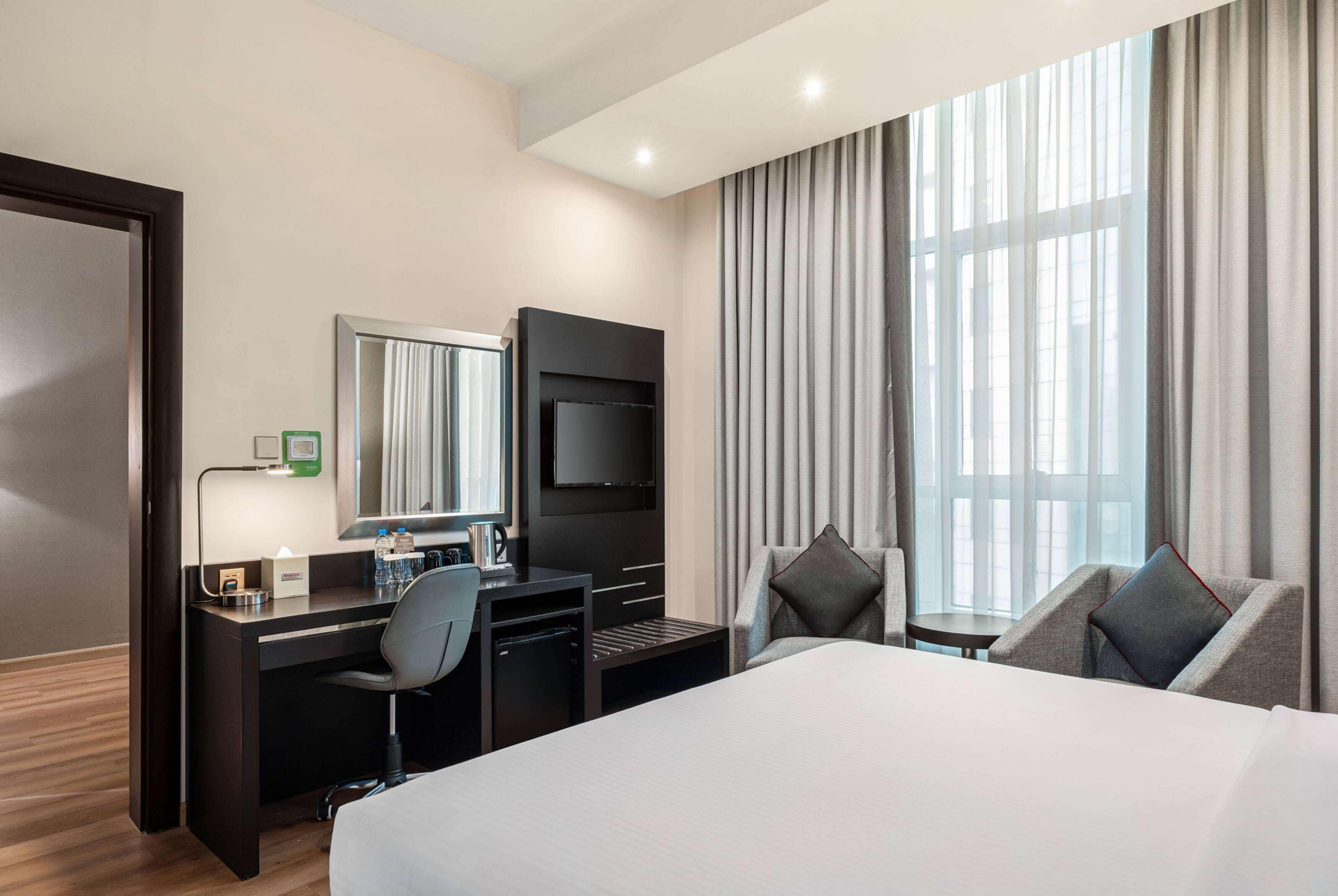 Une chambre d’hôtel avec un grand lit, un bureau avec une chaise, une télévision et une fenêtre avec des rideaux.