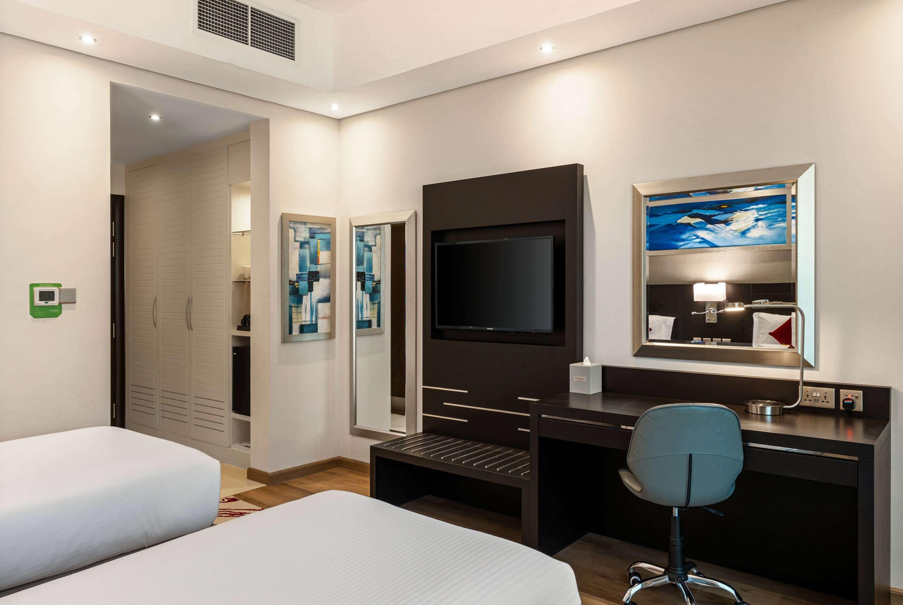 Une chambre d’hôtel avec deux lits, un bureau, une chaise, une télévision et des œuvres d’art accrochées aux murs.