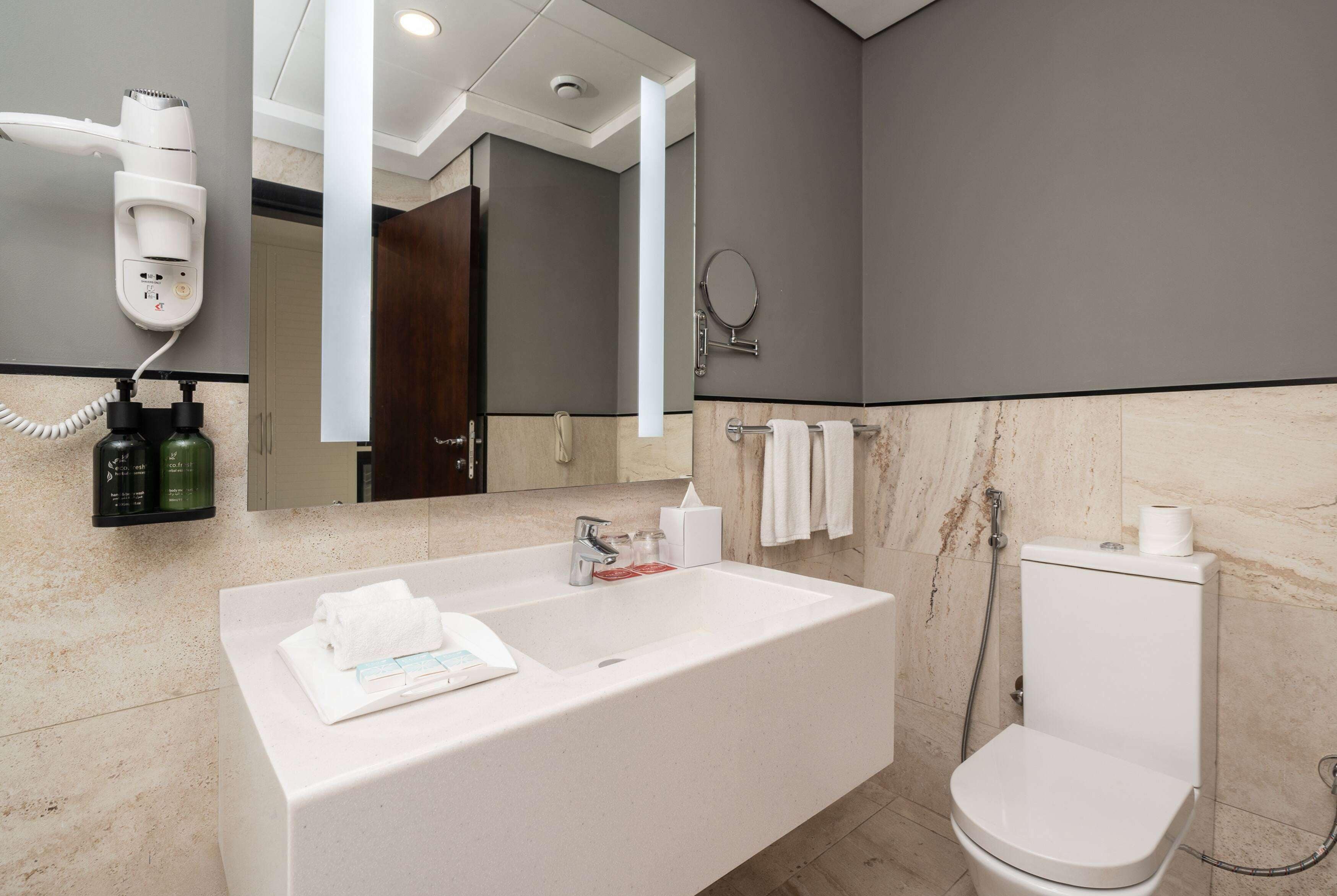 Une salle de bain moderne avec un grand lavabo blanc, un sèche-cheveux, un miroir et des toilettes.