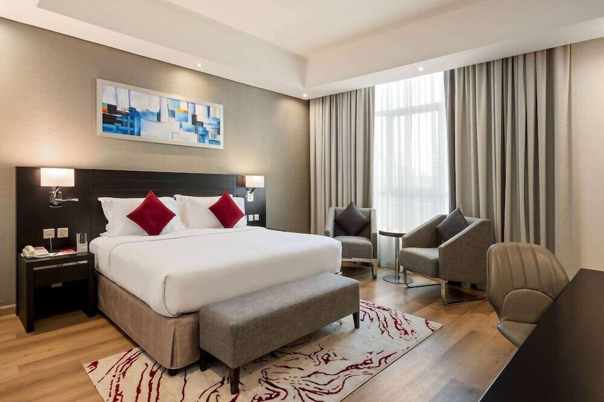 A hotel room with a large bed, two armchairs, a small table, and a painting on the wall.
