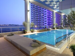A rooftop swimming pool with a view of a high-rise building, outdoor seating, and potted plants. - Ramada by Wyndham Dubai Barsha Heights (Dubai)