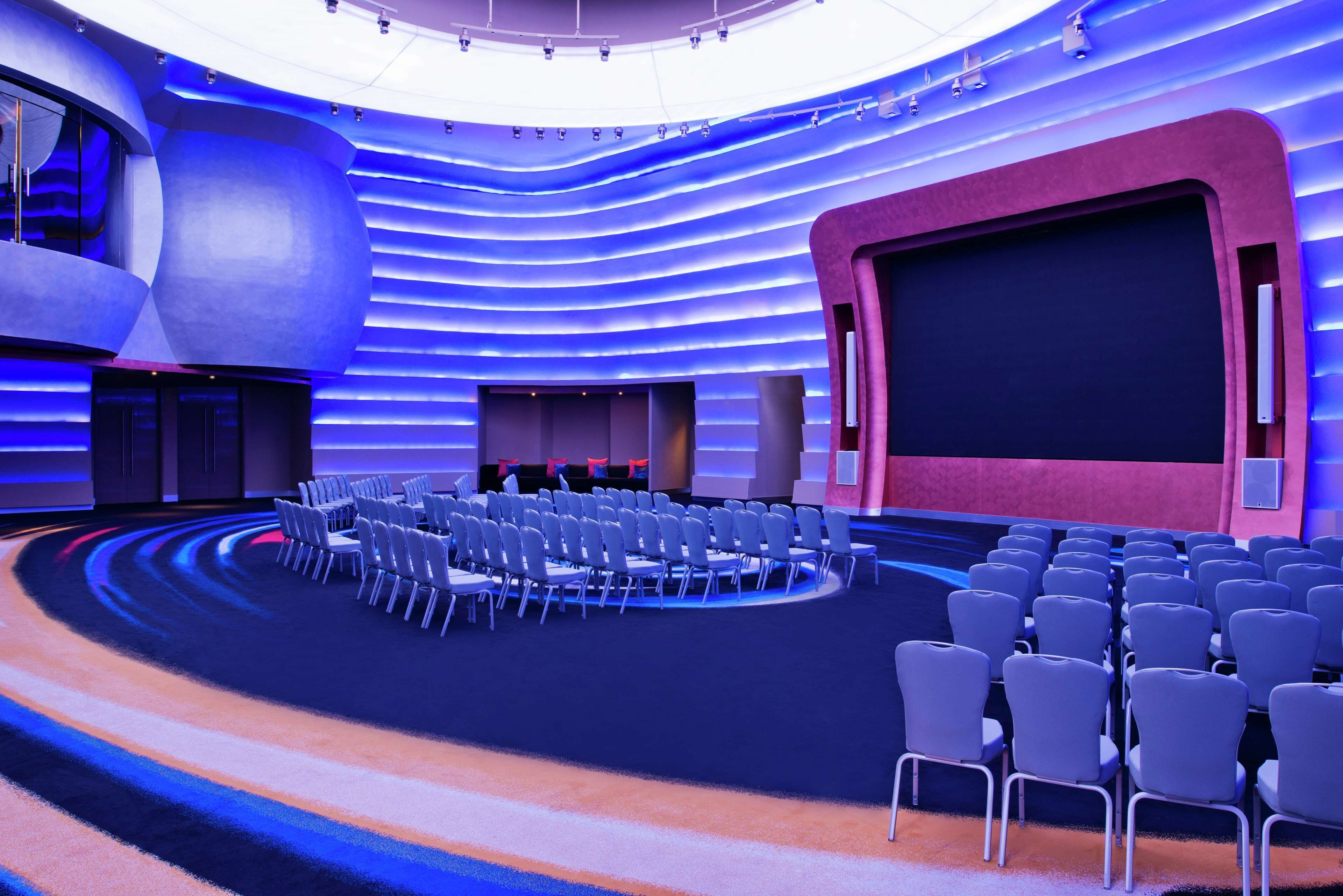 Un auditorio moderno con asientos en niveles, una pantalla grande y un escenario.