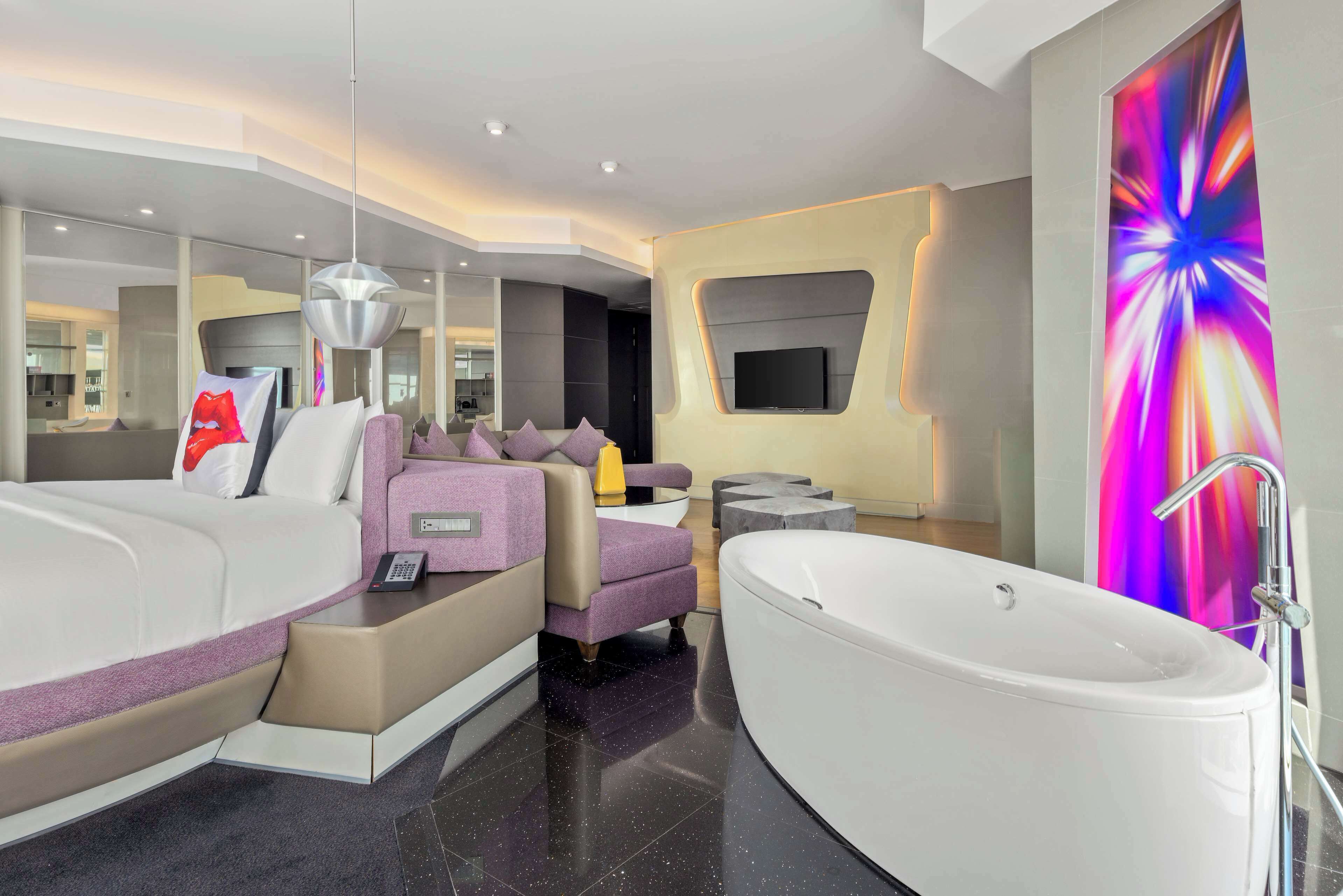 A modern bathroom with a large bathtub, a sofa, and a television mounted on the wall.