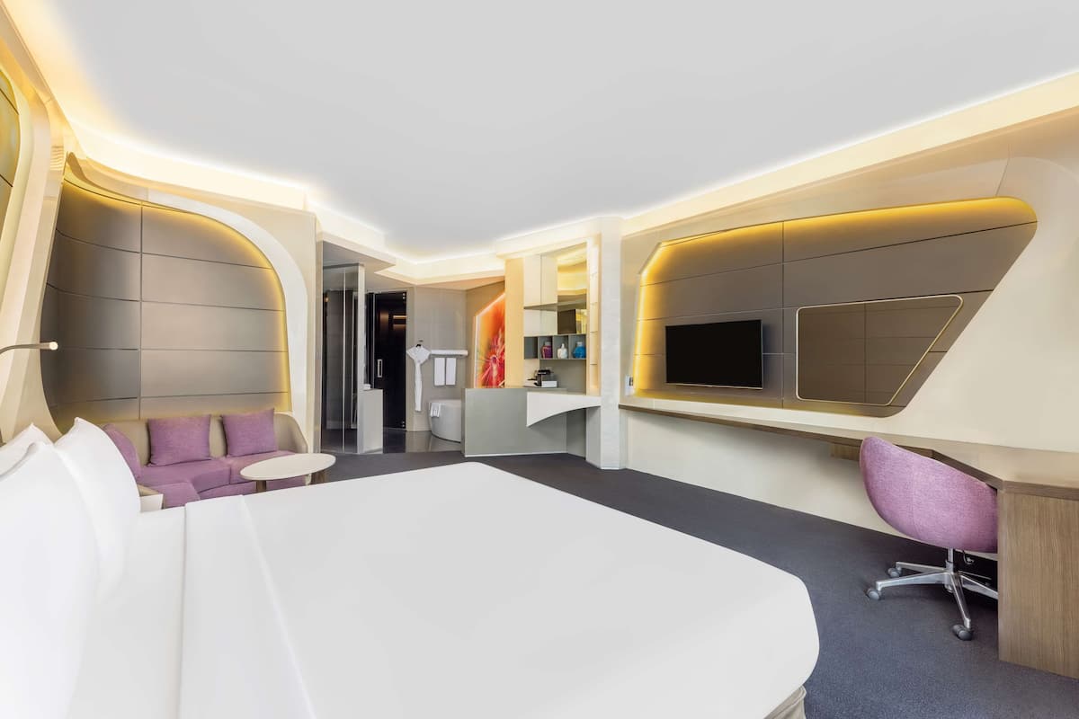 Una camera d'hotel moderna con un letto grande, una scrivania con un computer, un divano e una TV fissata al muro.