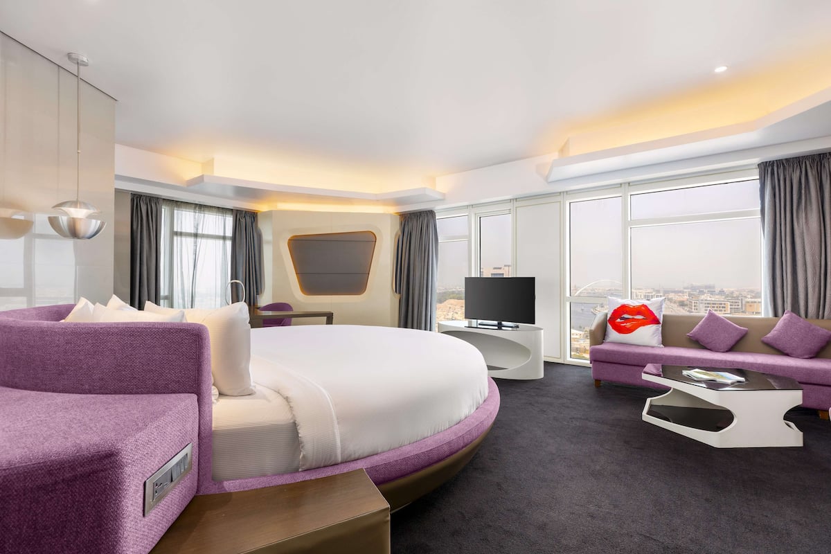 Una camera d'albergo moderna con un letto grande, un divano, una TV e vista sulla città.