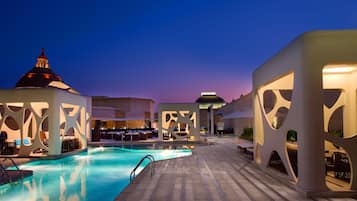 A pool area with lounge chairs and umbrellas, surrounded by modern architecture with unique cut-out designs.