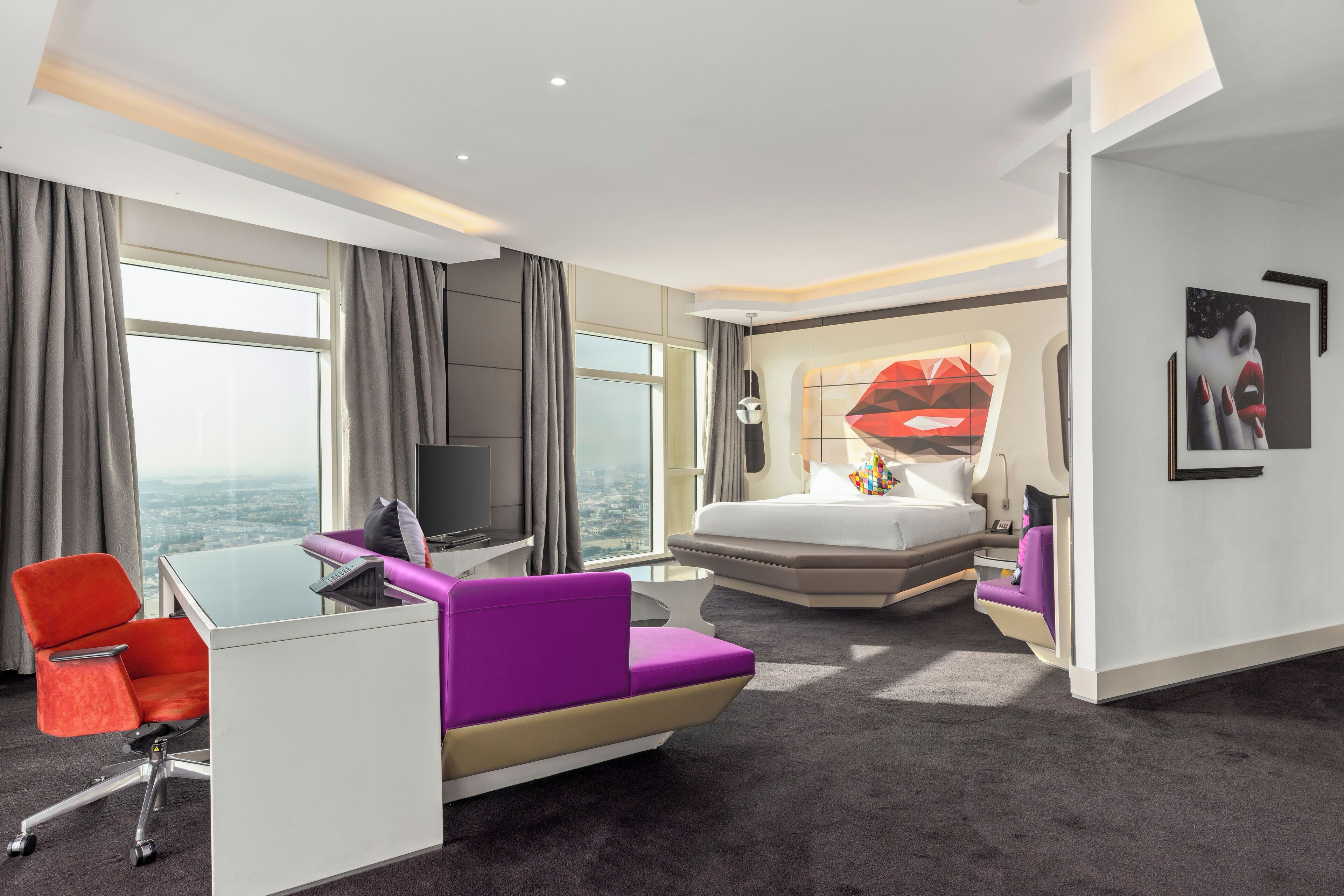A modern hotel room with a large bed, a desk with a chair, a sofa, and a television.