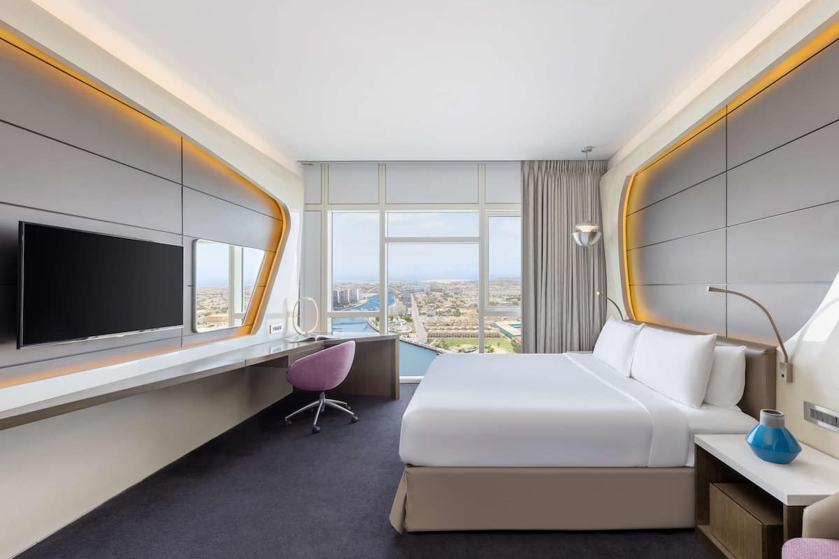 Una moderna camera d'hotel con un letto grande, una scrivania, una sedia, una televisione e vista sulla città.