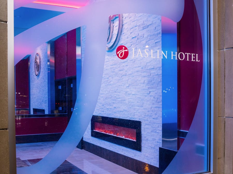 A modern interior with a prominent logo for JASLIN HOTEL, a stone accent wall, and a reflective floor.