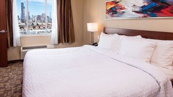 Quarto de hotel com uma cama grande, vista para a cidade, um quadro na parede e mesa de cabeceira com abajur.