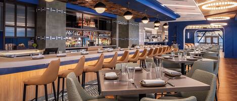 Een modern restaurant met een bar, meerdere tafels en stoelen.