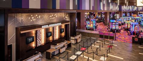 A hotel registration desk with a reception area, a row of gaming machines, and a patterned floor.