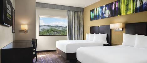 Habitación de hotel con dos camas, un escritorio, una silla, un ventanal con vistas a zonas verdes y un cuadro en la pared.