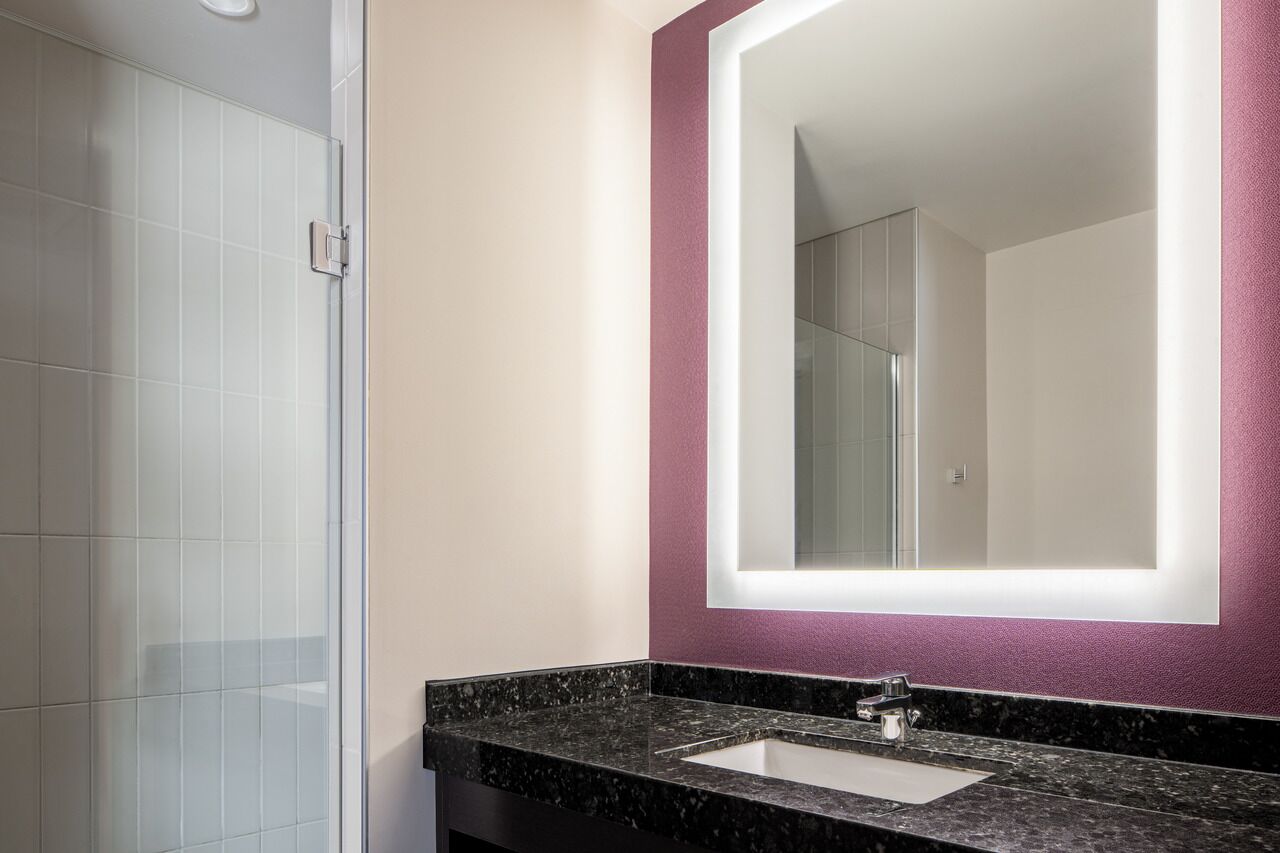 Un baño con lavamanos de mármol, un espejo grande y una cabina de ducha con paredes de vidrio.