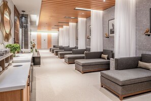 Ein modernes Spa mit grauen Sofas, Holzboden und einer Rezeption mit Theke und Pflanzen.