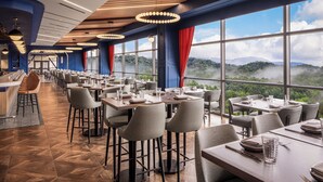 A restaurant with a long counter, multiple tables, and chairs, large windows with a mountain view. - Harrah's Cherokee Valley River Hotel & Casino – A Caesars Rewards Destination (Murphy)