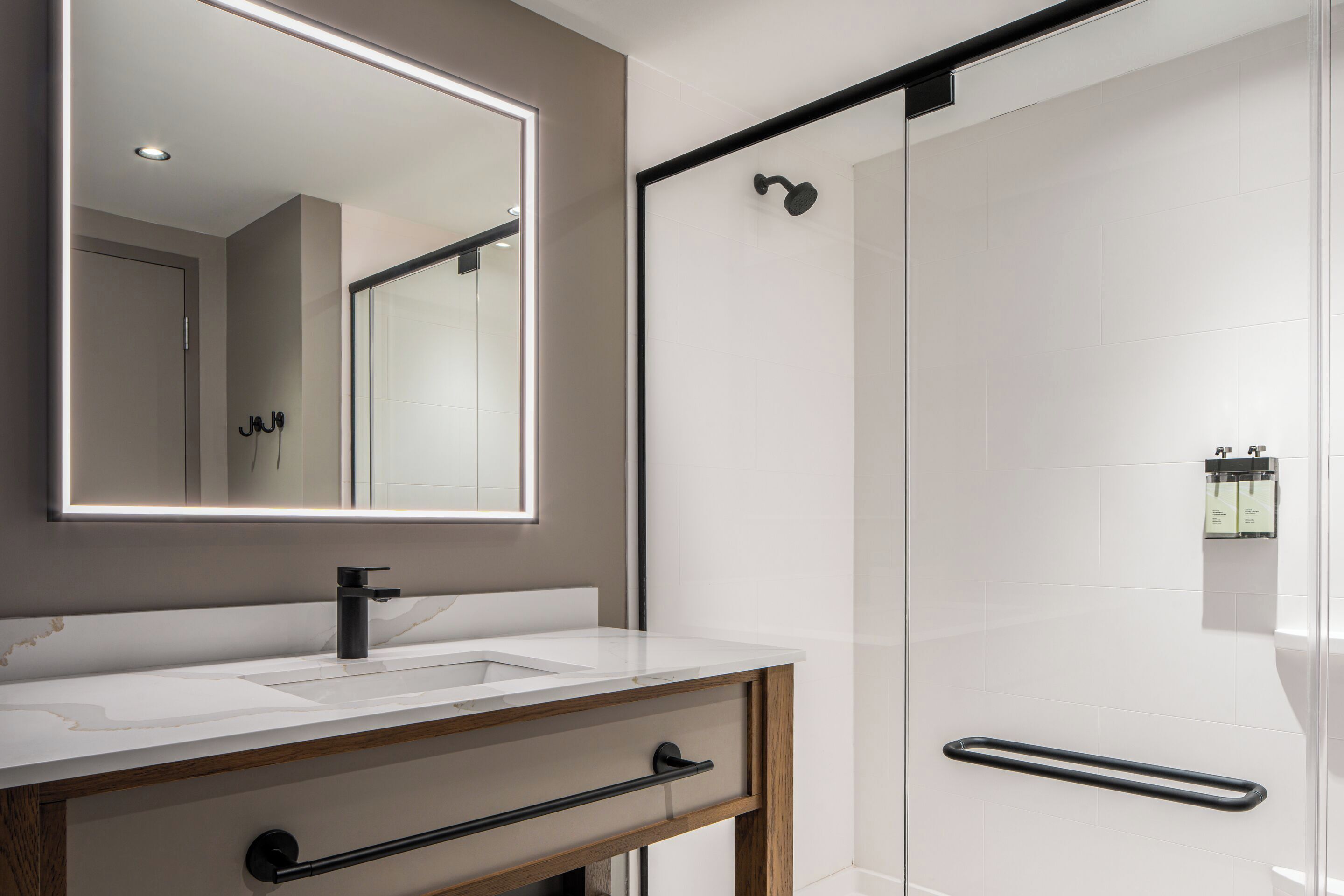 A modern bathroom with a large mirror, a sink, a shower, and a towel rack.