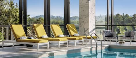 Zona de piscina con sillas de descanso, una columna de mármol y vistas a árboles y montañas.