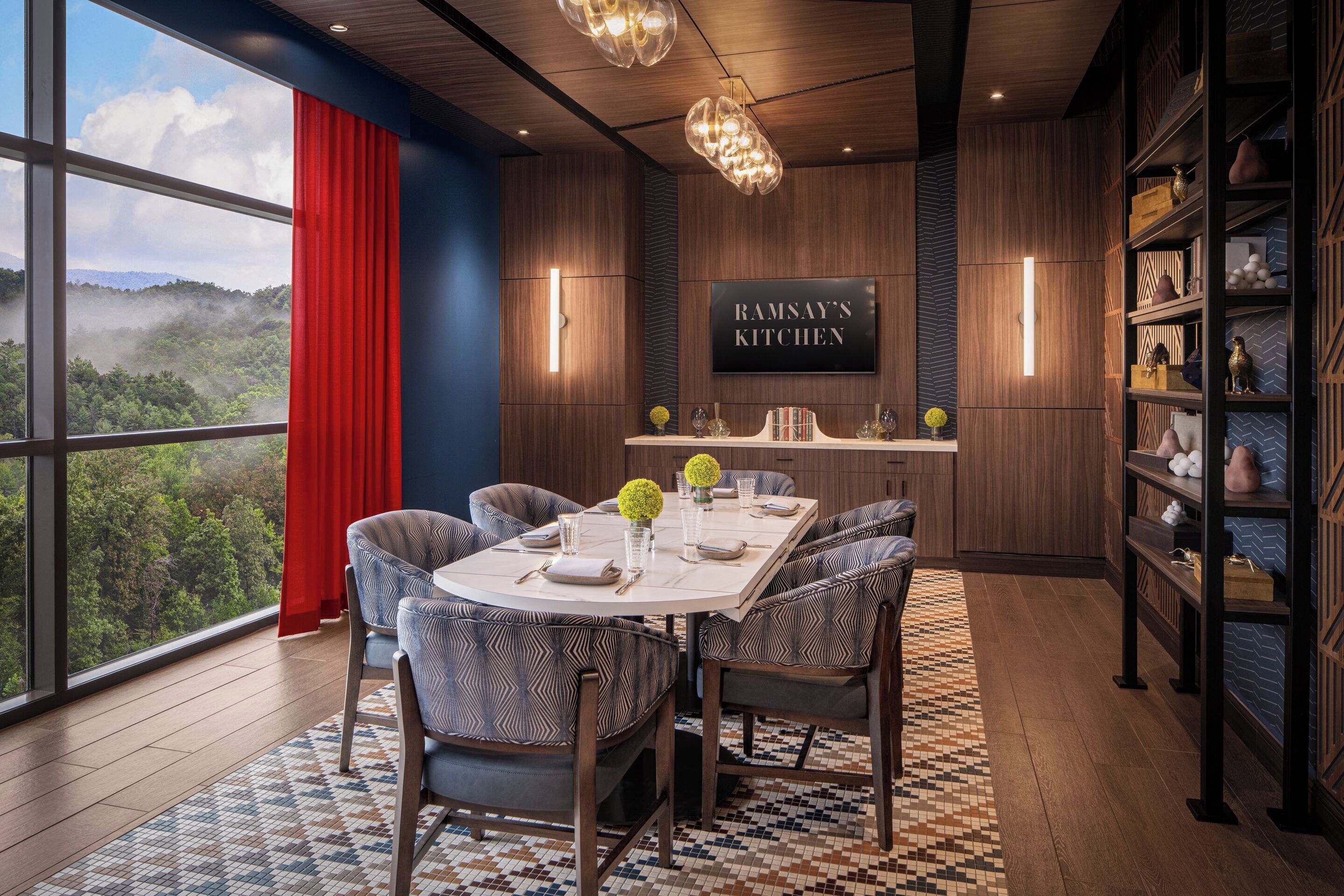 A modern kitchen with a large window, a dining area with patterned chairs, and a view of a forest.