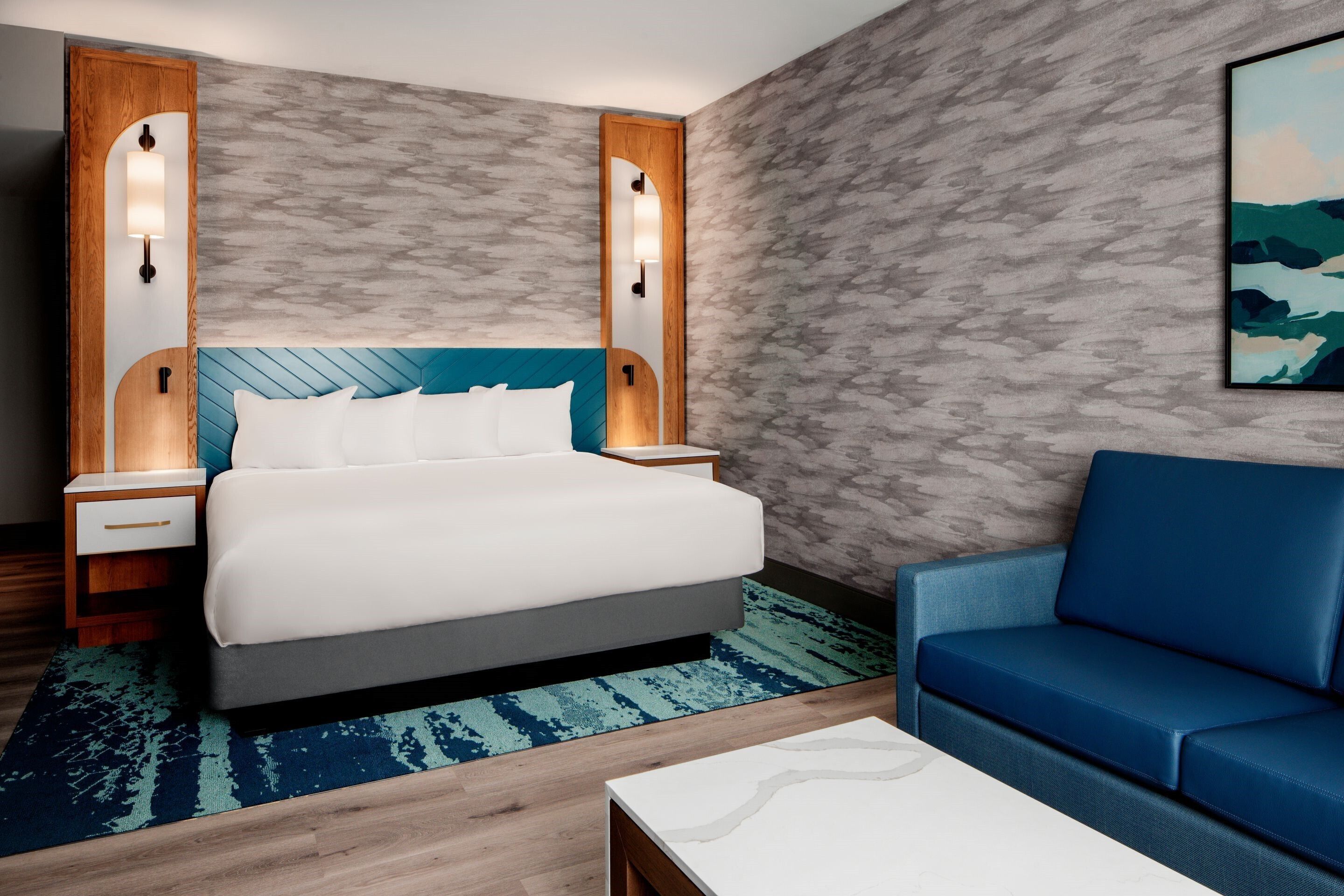 A hotel room with a bed, nightstands, a blue sofa, and a painting on the wall.