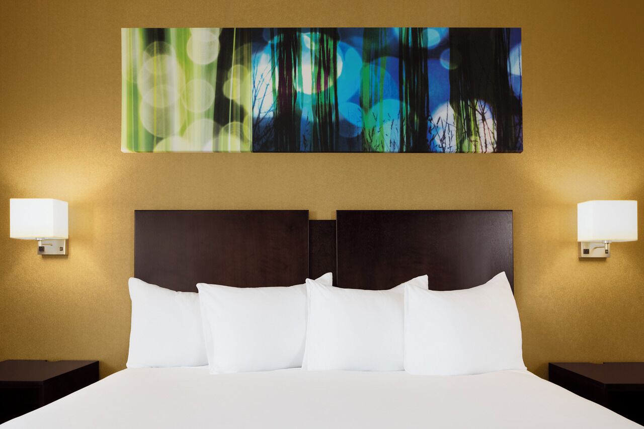 Habitació d'hotel amb un llit gran, dues taules de nit i un quadre abstracte penjat a la paret.