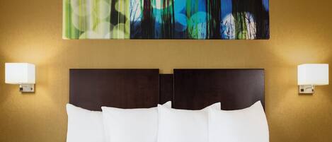 Une chambre d’hôtel avec un grand lit, deux tables de chevet et un tableau abstrait accroché au mur.