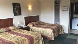 Habitación de hotel con dos camas, una mesita de noche, un teléfono, una lámpara fijada a la pared y una puerta que da a una kitchenette.