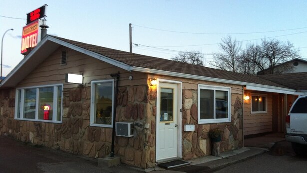 Un motel con fachada de piedra, un letrero de neón que dice 'OPEN' y una estructura de un solo piso.