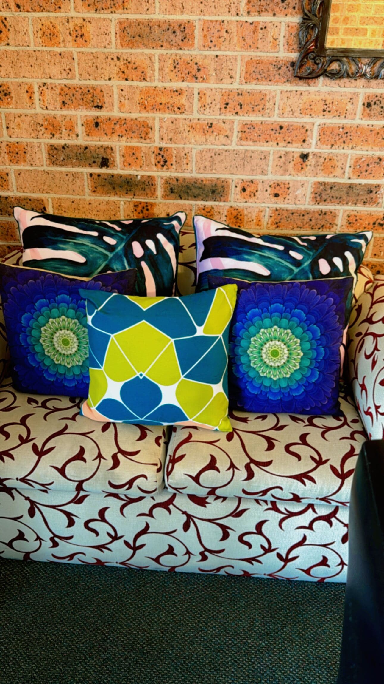 A sofa with patterned cushions against a brick wall.