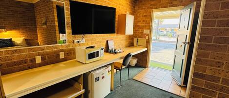 Una habitación de hotel compacta con kitchenette, una cama, un escritorio y un televisor.