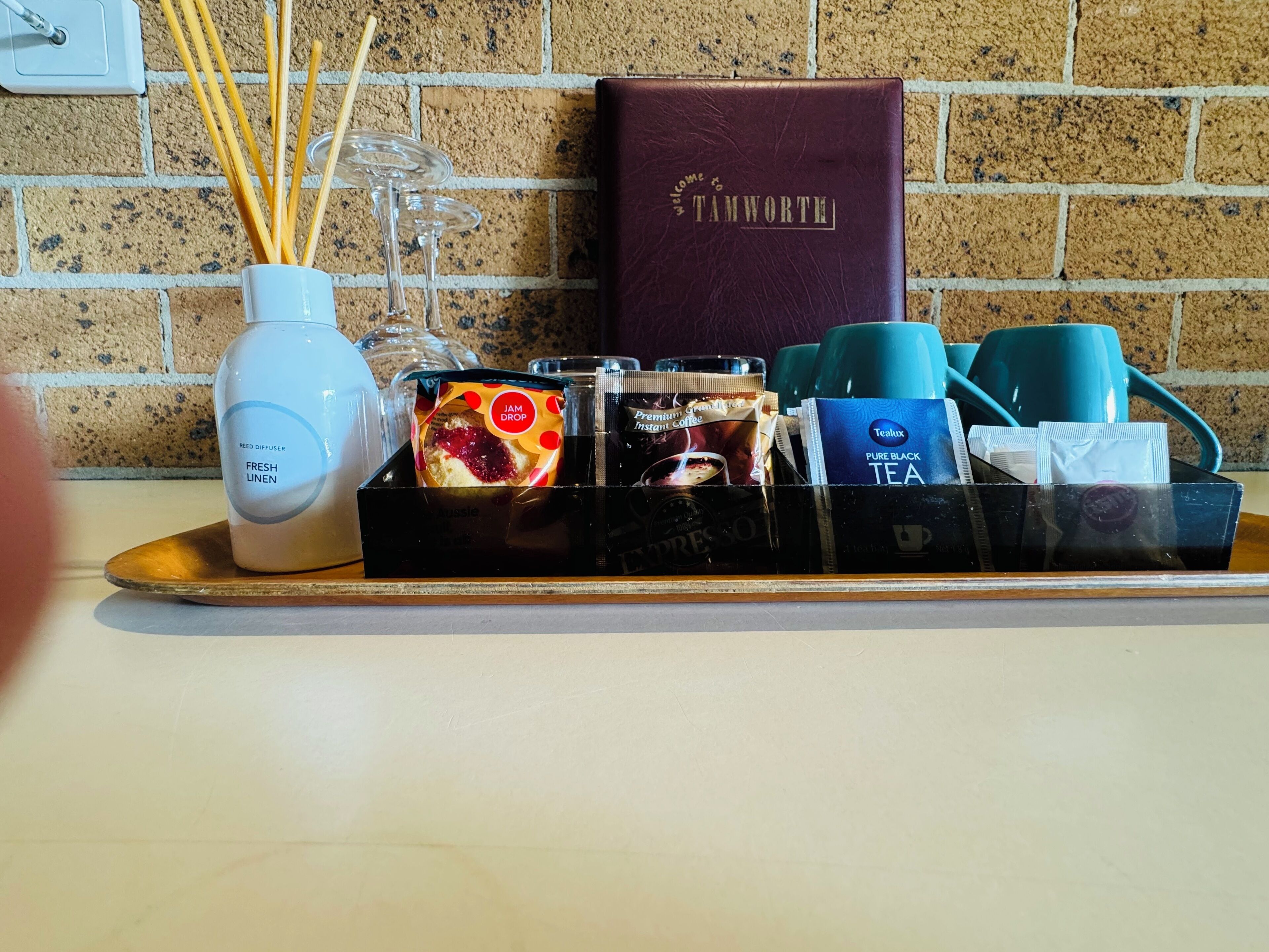 A tray with a reed diffuser, a jar of jam, instant coffee, and tea packets on a hotel counter.