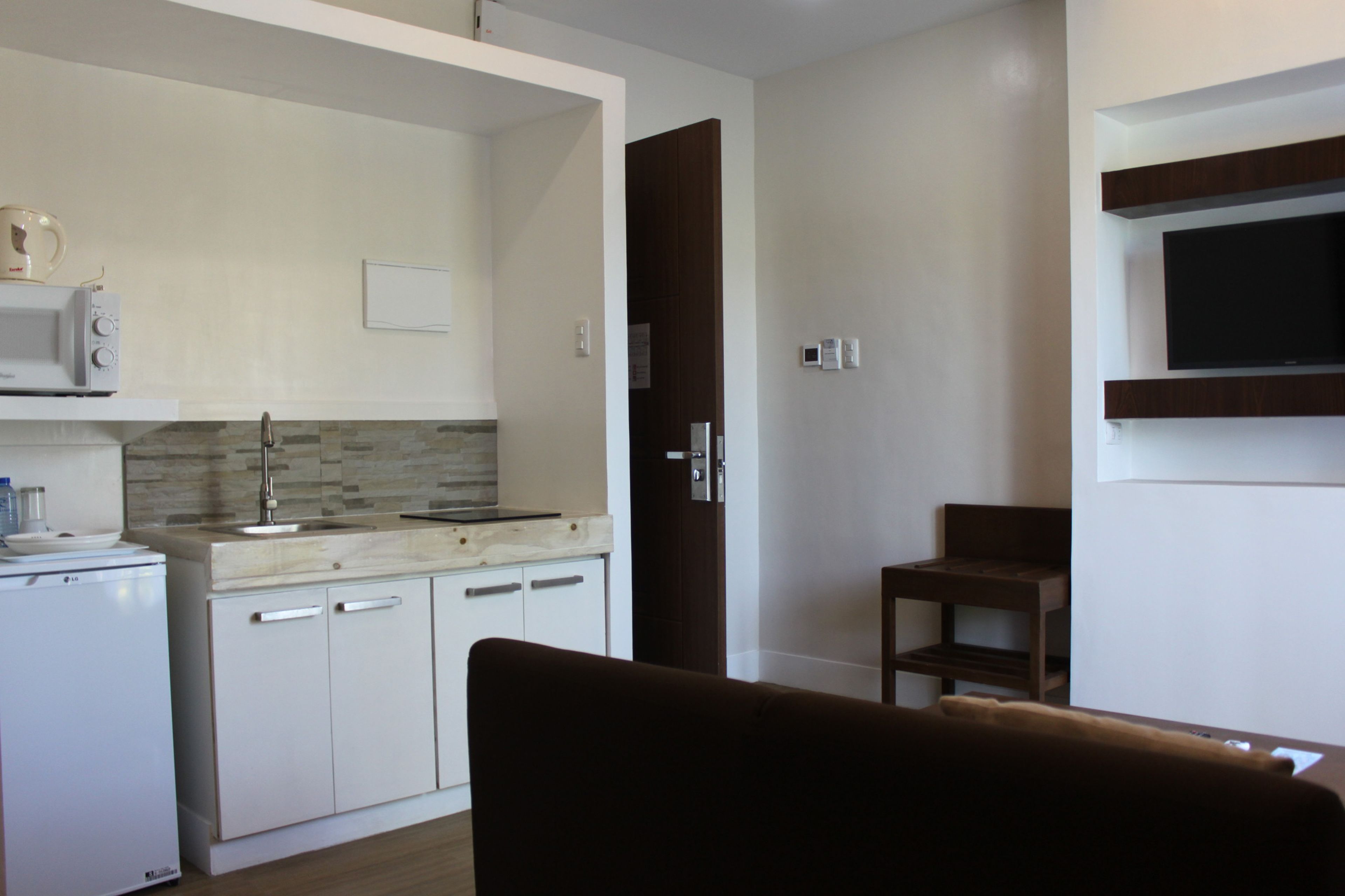 A compact kitchen with white cabinets, a microwave, and a coffee maker. There's a wooden door leading to another room.