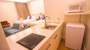 A compact hotel room with a kitchenette, a bed with blue and white bedding, a small seating area, and a microwave on a shelf. - The Reef Hotel and Residences (Olongapo)