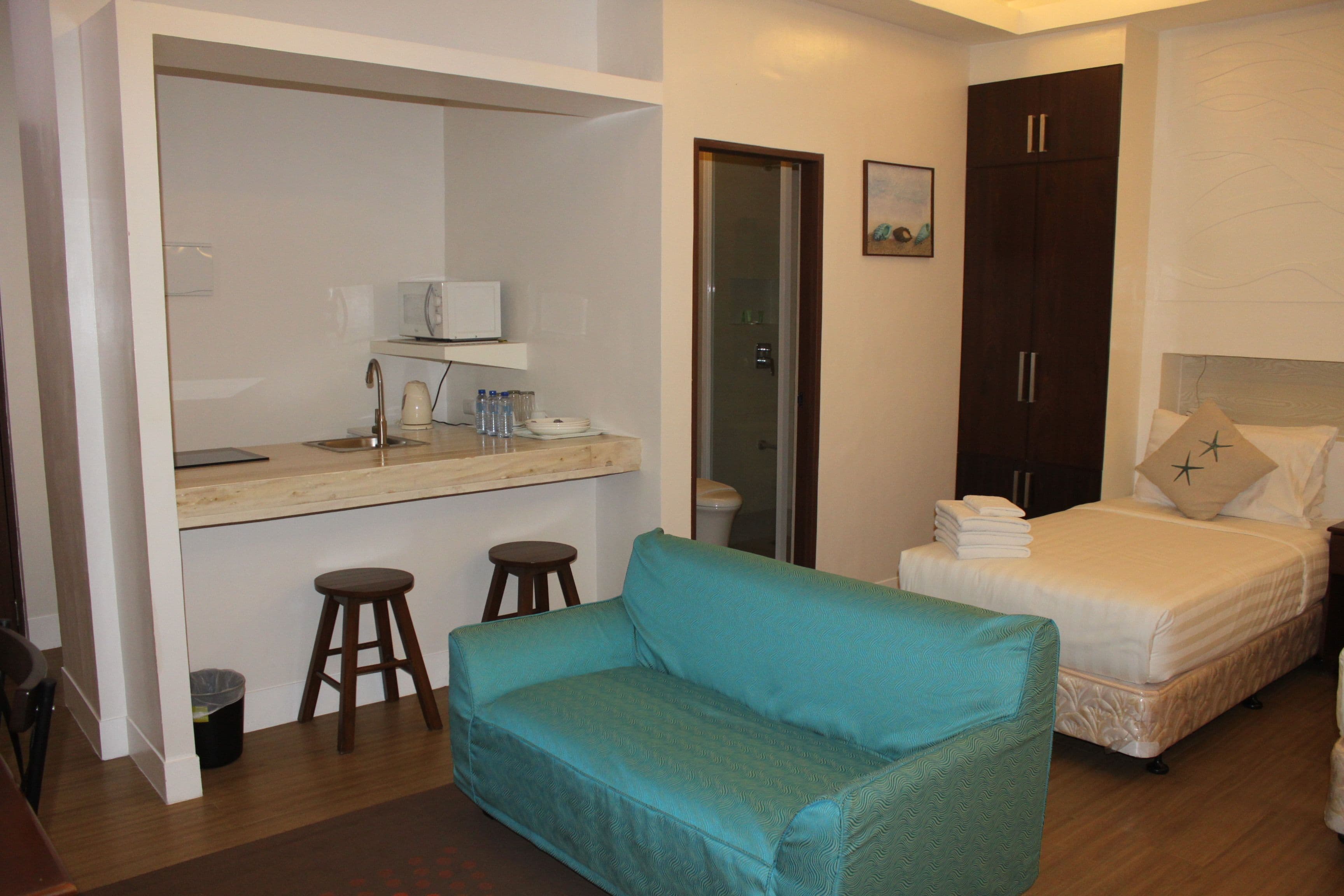 A compact hotel room with a kitchenette, a sofa, a bed, and a wardrobe.