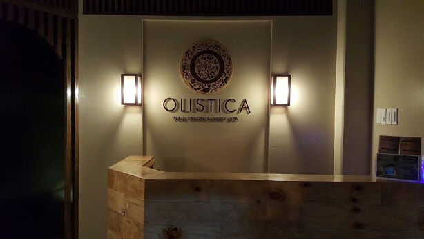 A reception desk with a wooden counter and a wall-mounted sign for 'OLISTICA NAIL SALON & BODY SPA'. - The Reef Hotel and Residences (Olongapo)