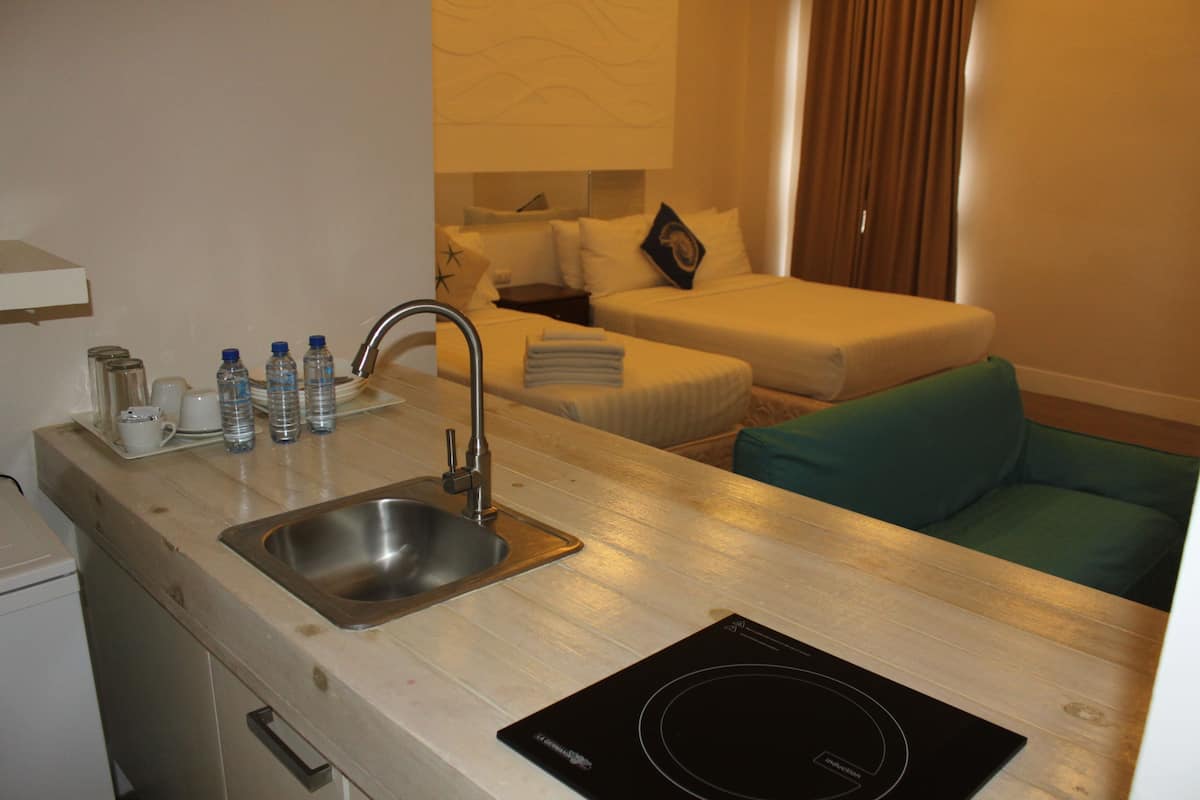 A hotel room with a kitchenette, a sink, a stove, a bed, and a green chair.