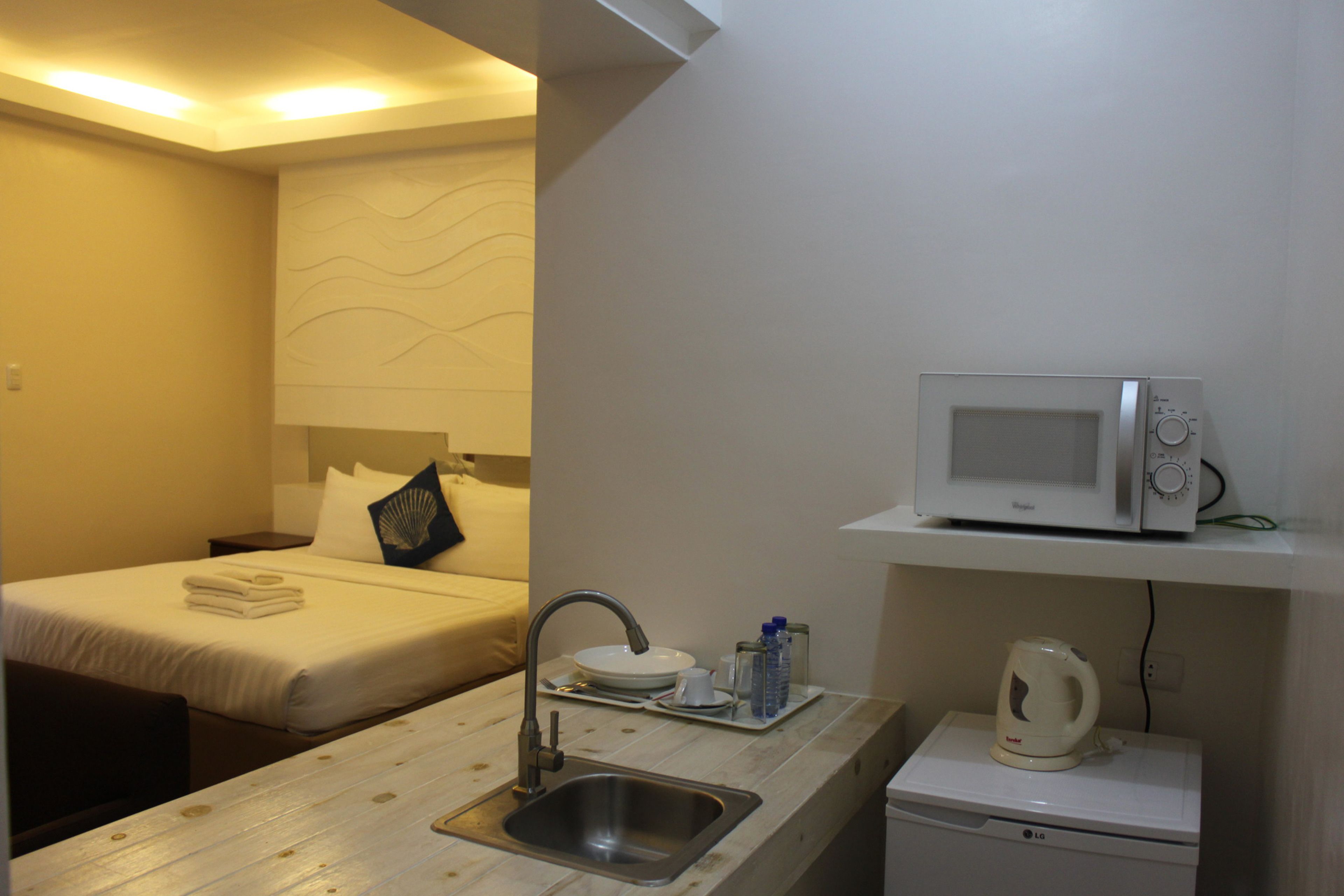 Habitación de hotel compacta con kitchenette, cama, lavamanos y microondas.