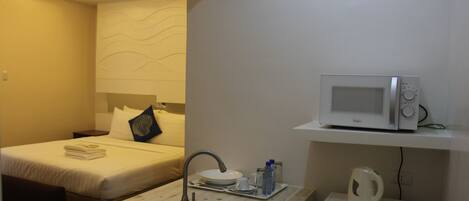 A compact hotel room with a kitchenette, a bed, a sink, and a microwave.