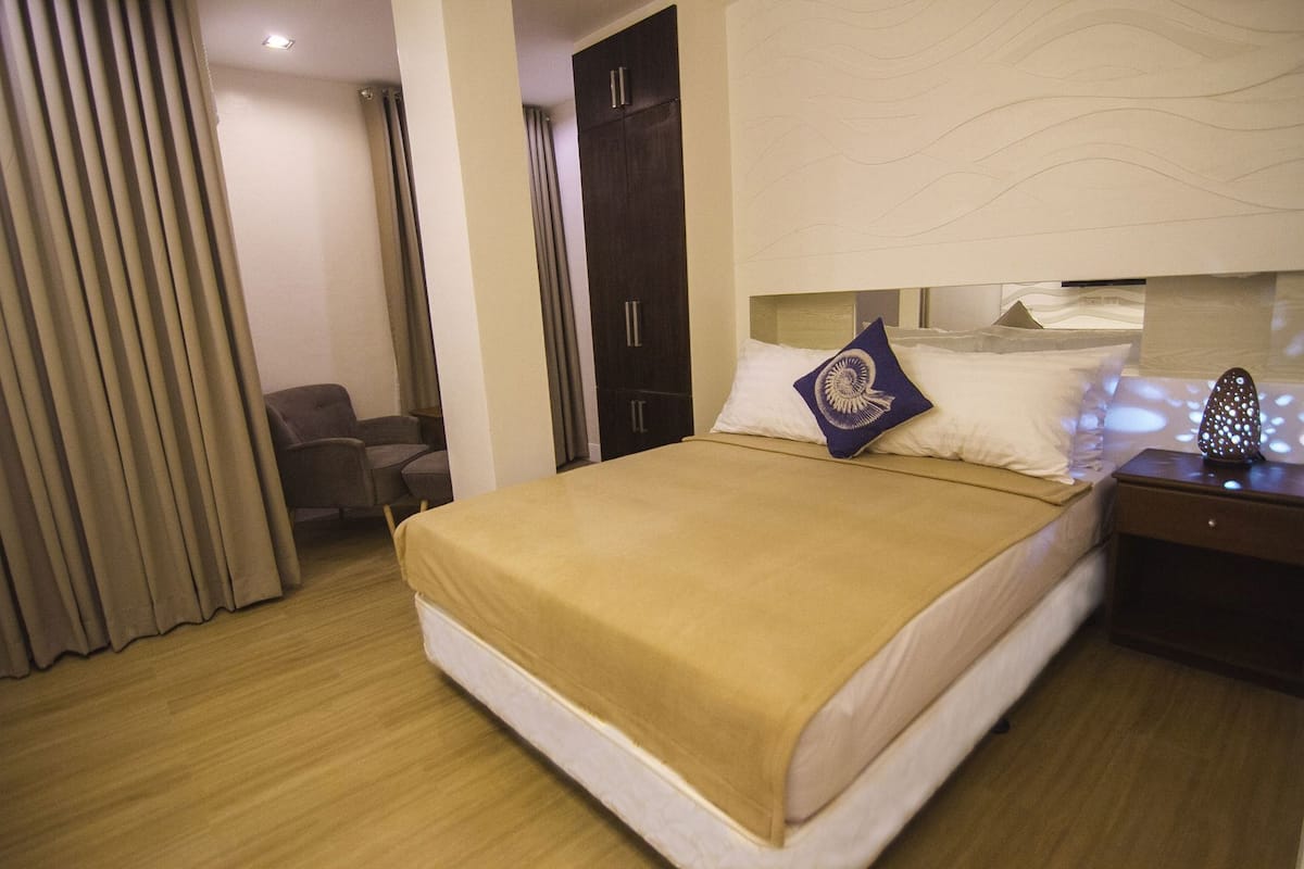 A hotel room with a bed, a nightstand, a chair, and a wardrobe.