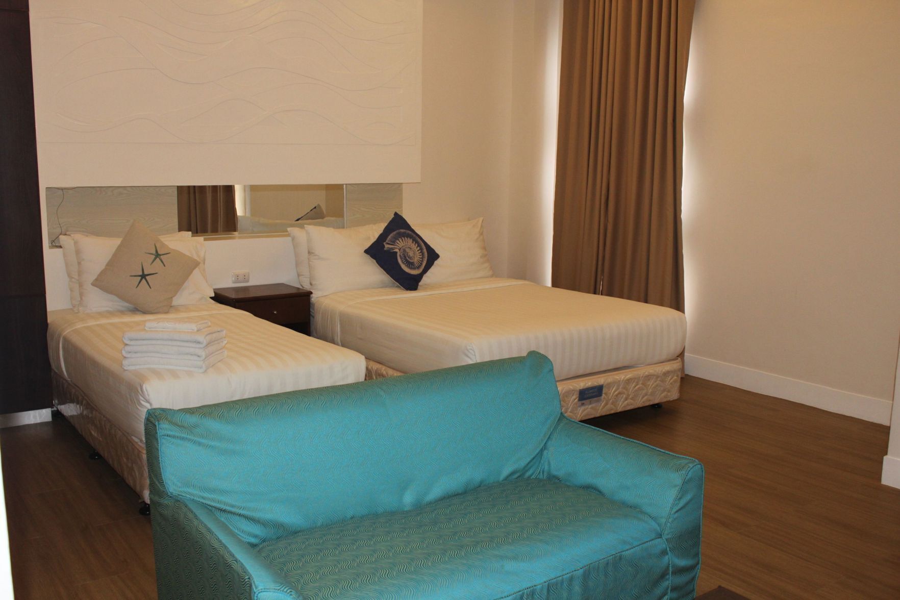A hotel room with two beds, a teal armchair, and a large window with curtains.