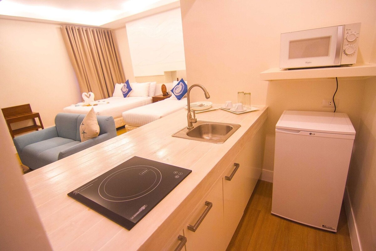 A hotel room with a kitchenette, a microwave, a refrigerator, a sink, a dining table, and a bed with blue and white bedding.