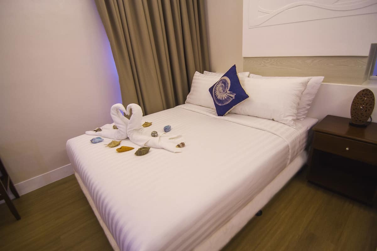 A neatly made bed with white linens, a blue decorative pillow, and a towel arrangement on the bed.