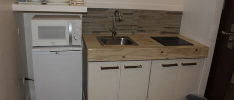 A compact kitchenette with a microwave, sink, and wooden countertop.