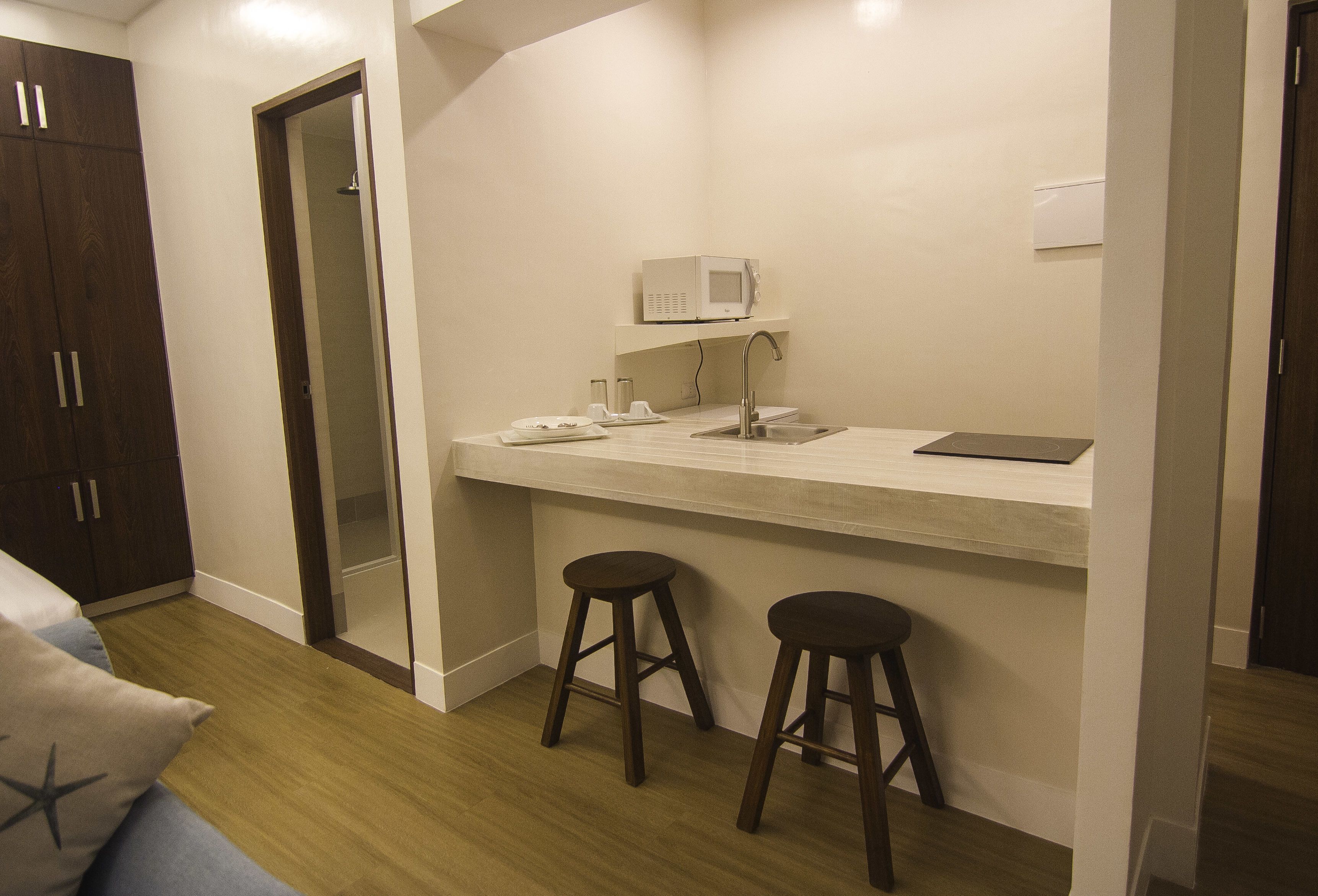 A compact room with a kitchenette, a microwave, two stools, a small table, and a cabinet.