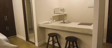 A compact room with a kitchenette, a microwave, two stools, a small table, and a cabinet.