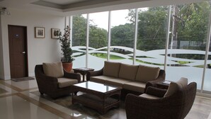 A spacious lobby with a large window offering a view of greenery outside. There is a brown wicker sofa set, a glass coffee table, and a potted plant. - The Reef Hotel and Residences (Olongapo)