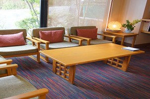 Una habitación con una mesa de madera, cuatro sillas acolchadas, una mesita de noche con una lámpara y una planta en maceta.