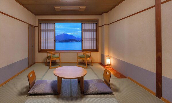 Una habitación japonesa tradicional con suelo de tatami, una mesa baja, dos sillas, una ventana con paneles shoji y una luz nocturna.